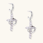 White gold-plated hoop earrings with sparkling zirconia cross charms dangling against cream background