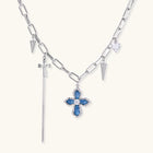White gold plated chain necklace with blue textured cross pendant, spike charms, and mini cross detail on beige background