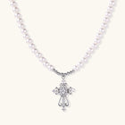 Ornate scrollwork cross pendant with zirconia stones on a strand of glossy white beads and silver-tone bead accents.