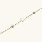 Gold chain bracelet with white mother of pearl butterfly pendant and two bezel-set crystals on cream background